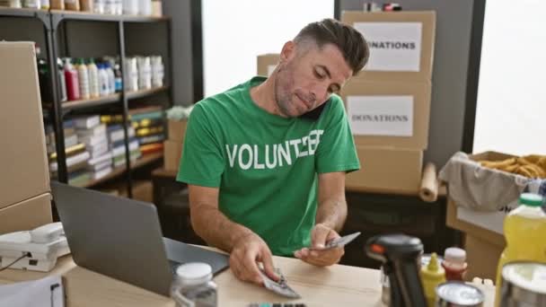 Knappe jonge Spaanse man die vrijwilligerswerk doet, donatiedollars telt terwijl hij bezig is met een oprecht gesprek op zijn smartphone in het liefdadigheidscentrum - Video
