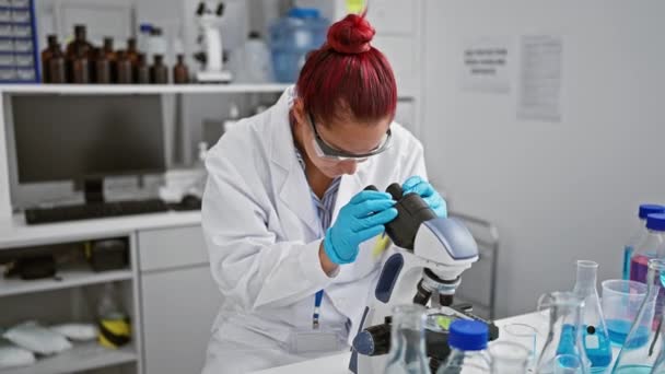 Usmívající se mladá zrzka žena vědec sebevědomě pomocí mikroskopu v laboratoři, sedí se zkříženýma rukama v gestu objevu a analýzy. - Záběry, video