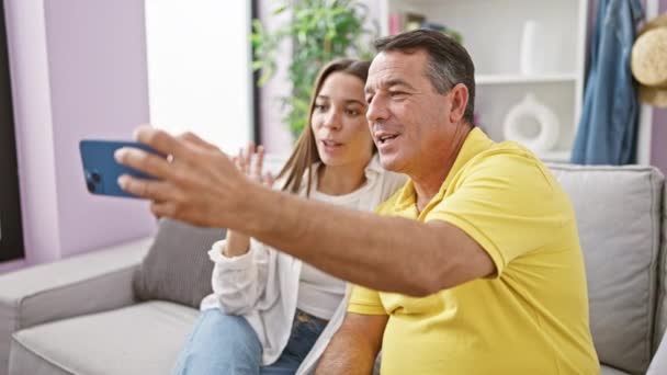 Hartverwarmende scène van een vader en dochter blij zittend op de bank thuis, diep in gesprek tijdens een gezellig indoor videogesprek, hun liefde en positieve familierelatie etalerend. - Video