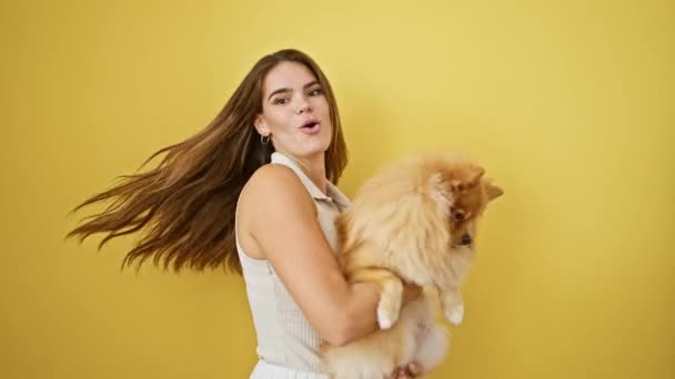 Zářící mladá hispánská žena objímající svého hravého psa, sebevědomě stojící proti zářivému izolovanému žlutému pozadí, ztělesňujícímu radost a pozitivitu. - Záběry, video