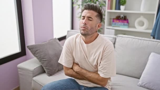 Homem hispânico jovem preocupado, retrato da doença, sofrendo dor de estômago intensa enquanto infelizmente descansa, deitado no sofá da sala de estar, dentro de casa, em casa - Filmagem, Vídeo