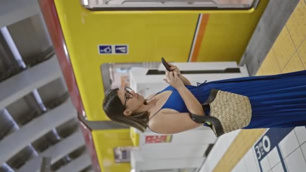 Alegre mujer hispana vestida de gafas inmersa en un sonriente viaje telefónico, absorbiendo vibraciones de la ciudad mientras está parada en la plataforma de la estación de metro de ginza esperando su tren de viaje. - Imágenes, Vídeo