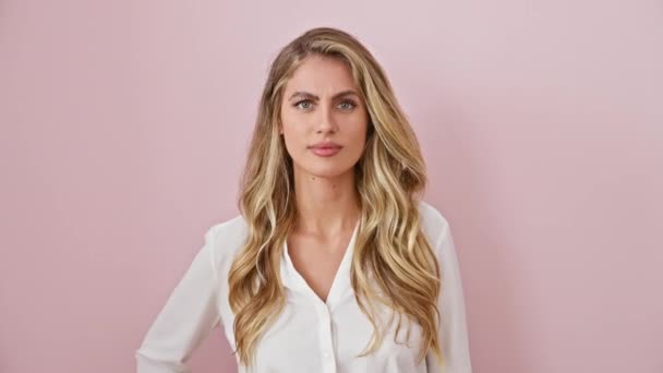 Verbaasde jonge vrouw in shirt staan over roze achtergrond, haar blonde schoonheid versterkt door een geschokte uitdrukking van ongeloof en verbazing, handen op kin. - Video