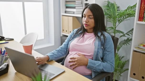 Jong verwacht moeder aanraken van haar buik tijdens het werken op laptop, een succesvolle en vastberaden zakelijke professional op kantoor - Video