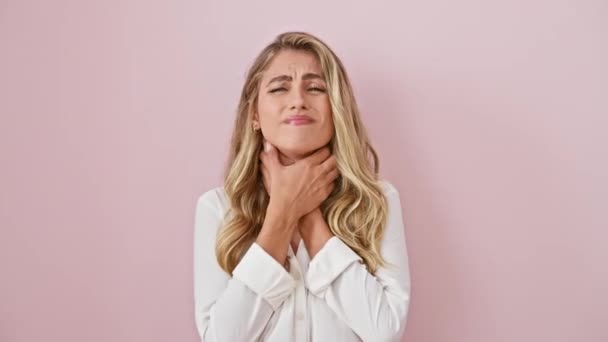 Jonge blonde dame in pijn, die haar pijnlijke keel vastklemt zoals griep en infectie symptomen laten zien, staande tegen een geïsoleerde roze achtergrond, met een gebroken uitdrukking - Video
