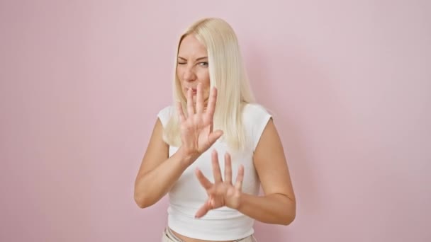 Obrzydliwa blondynka, młoda kobieta wykazująca awersję, przerażająco gestykulująca dłońmi nad odizolowanym różowym tłem - Materiał filmowy, wideo