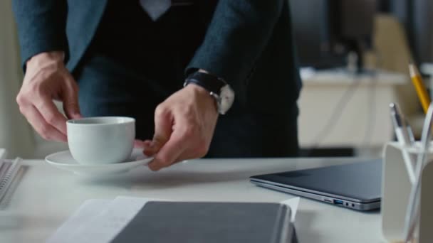 Puukotettu kuva tunnistamattomasta liikemiehestä puvussa tuomassa kahvia työpaikalle ja jatkamassa työskentelyä kannettavan tietokoneen parissa - Materiaali, video