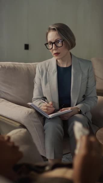 Vertical selective focus shot of female psychologist listening to her patient lying on couch - Footage, Video