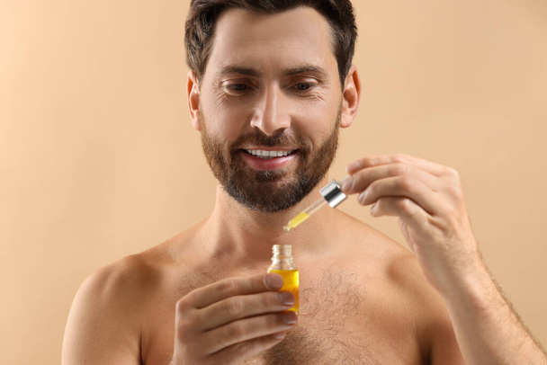 Smiling man with cosmetic serum on beige background, closeup - Zdjęcie, obraz
