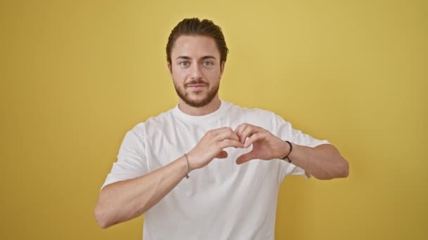 Jeune homme hispanique souriant confiant faire geste de coeur avec les mains sur fond jaune isolé - Séquence, vidéo
