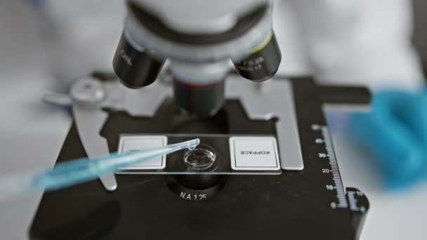 Atractivo joven hispano, científico de pelo gris en el trabajo, vertiendo una gota sobre una muestra usando el microscopio en un experimento de laboratorio - Metraje, vídeo