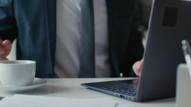 Ofiste dizüstü bilgisayarla çalışırken takım elbiseli, kahve içen tanınmamış bir ofis çalışanının yakın plan fotoğrafı. - Video, Çekim