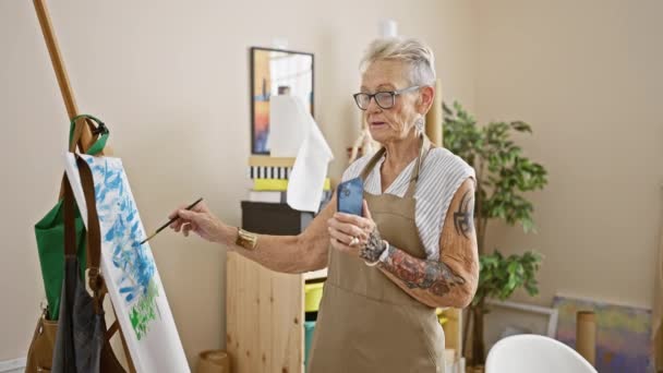 Charming grey-haired senior woman artist dazzles in her art studio, skillfully drawing and engaging in a lively video call lesson with a middle-aged student, capturing creativity and fun. - Footage, Video