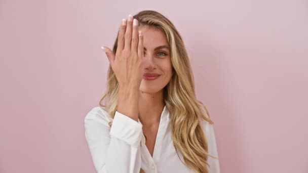 Brutale peekaboo, aantrekkelijke jonge vrouw vol vertrouwen bedekken van een oog, gekleed in shirt tegen geïsoleerde roze achtergrond knipperen een vrolijke glimlach - Video