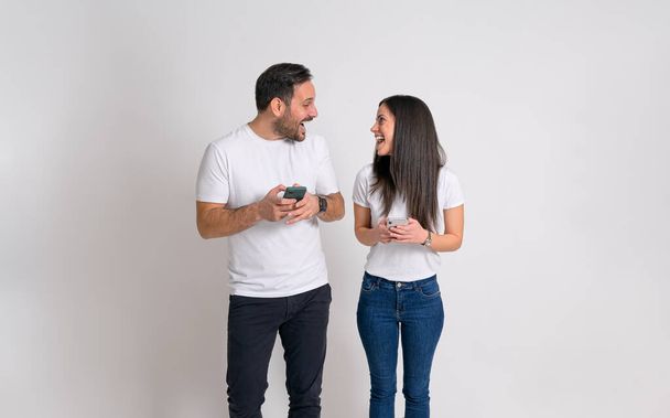 Nadšený pár s mobily dívá na sebe a křičí extaticky na bílém pozadí - Fotografie, Obrázek