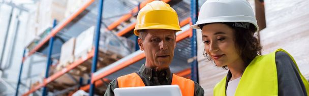 happy supervisor in hard hat holding tablet while explaining work to employee in warehouse, banner - Photo, Image