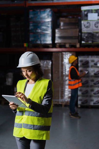 female warehouse employee in hard hat using table with a male colleague on blurred background - Photo, Image