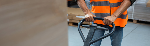cropped banner of warehouse worker in hard hat and safety vest transporting pallet with hand truck - Photo, Image