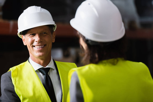 happy middle aged supervisor looking at his female colleague in hard hat on blurred foreground - Photo, Image