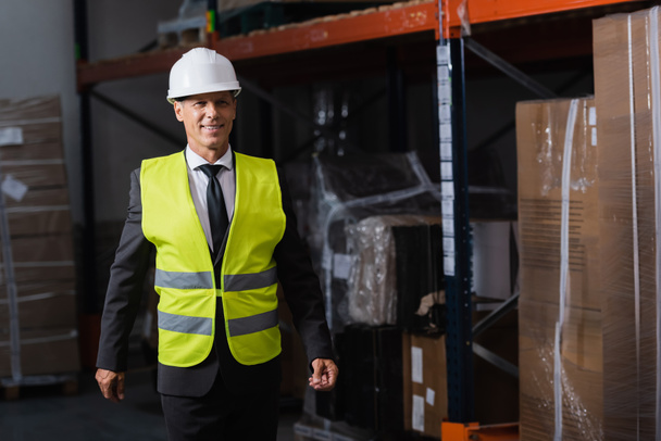 Smiling man in safety vest and hard hat and safety vest walking in warehouse, professional headshot - Photo, Image