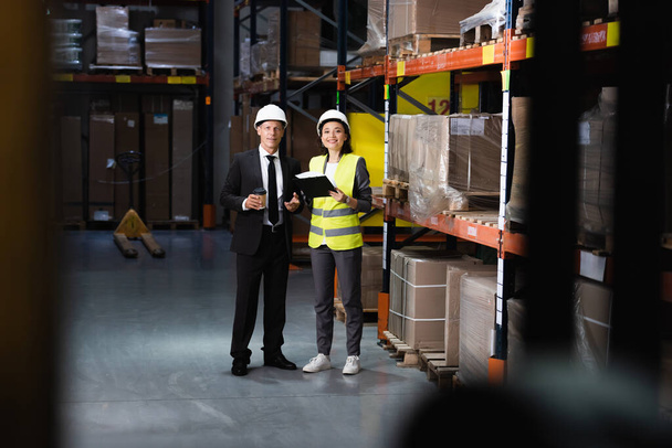 hymyilevä liikemies puku ja kypärä keskustella logistiikan operaatioista naispuolisen työntekijän kanssa - Valokuva, kuva