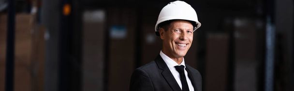 happy middle aged businessman in hard hat and suit smiling warehouse, professional banner - Photo, Image