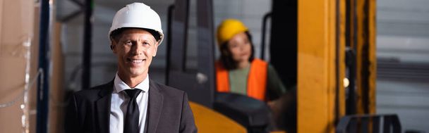 supervisor de armazém de idade média em terno e chapéu duro sorrindo enquanto olha para a câmera, banner - Foto, Imagem