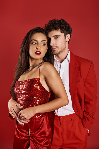 elegant young couple in evening attire hugging during romantic date on Valentines day, red backdrop - Photo, Image