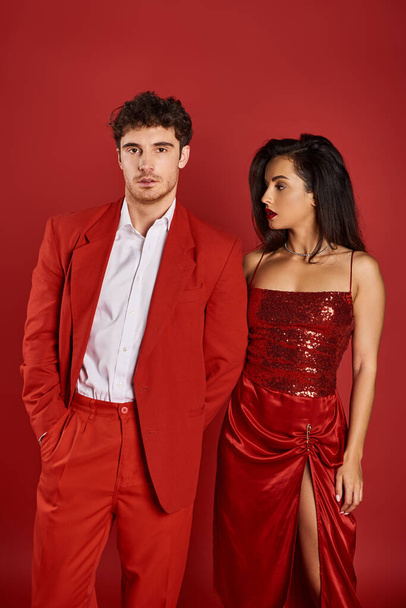 elegante joven con labios rojos seduciendo hombre guapo posando sobre fondo rojo, mano en bolsillo - Foto, imagen