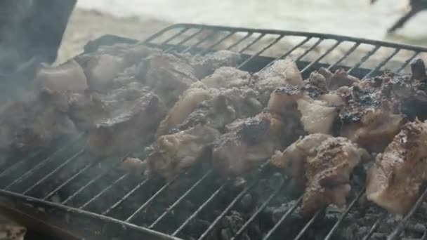 muž kontroluje kousky masa z vepřového krku vidličkou na grilu, na břehu řeky - Záběry, video