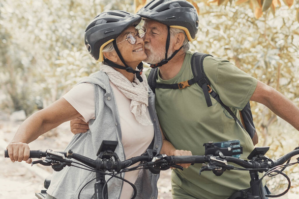 Пара милих і милих літніх людей в любові насолоджуються разом природою на відкритому повітрі, розважаючись з велосипедами. Старий цілує свою дружину посміхаючись і відчуваючи себе добре
. - Фото, зображення