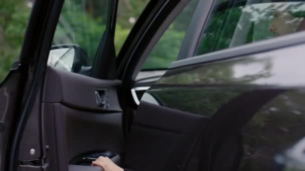 Średni widok z tyłu człowieka kaukaskiego otwierającego drzwi kierowcy i wysiadającego z czarnego samochodu w strefie parkingowej - Materiał filmowy, wideo