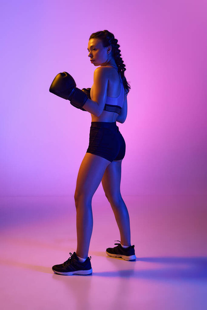 Sporty elegance portrait of strong female boxer, professional MMA sportsman against gradient pink-violet studio background in neon light. Concept of sport, active lifestyle, health, competition. - Photo, Image