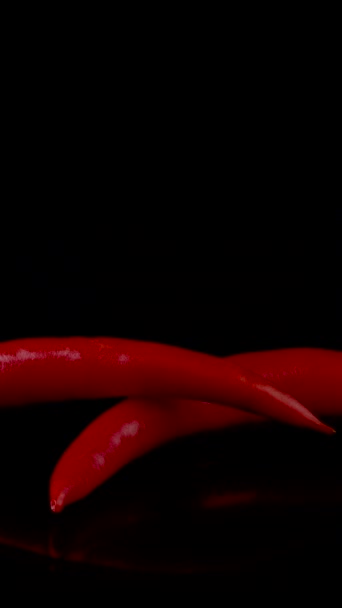 Hete rode chili pepers in vlammen op een zwarte achtergrond. Pittig voedselconcept. Close-up, verticale beelden - Video