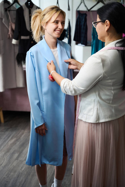 Femme souriante ayant un essayage dans un atelier de couture, le maître utilise des gadgets à coudre - Photo, image