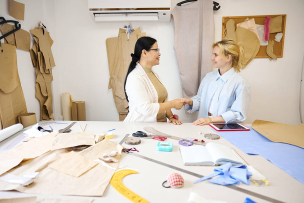 Mistrz krawiectwa wita projektantkę mody w jej miejscu pracy, kobiety stoją przy stole do krojenia - Zdjęcie, obraz