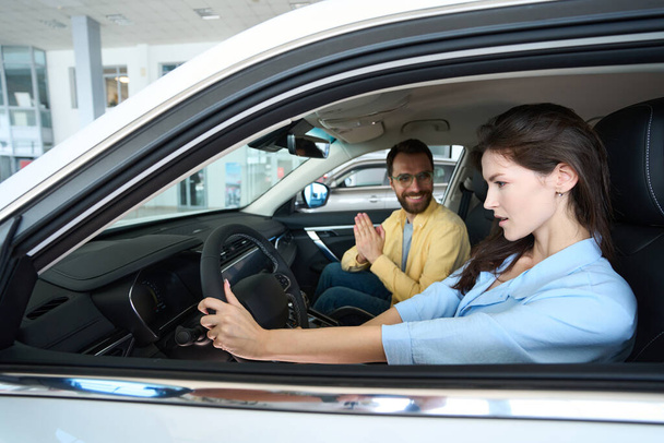 Beautiful woman holding steering wheel while sitting in auto with her boyfriend in car center - Photo, Image