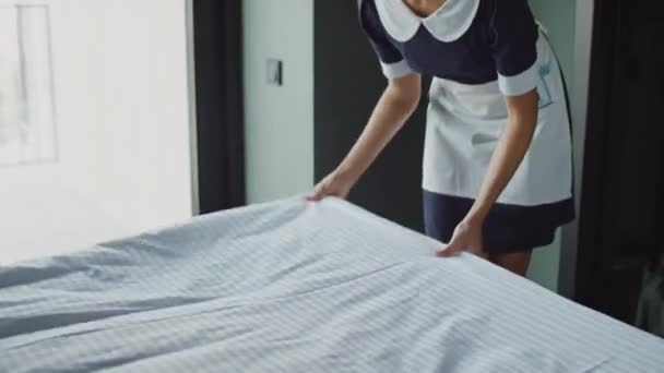 Medium wide shot of female room attendant making bed in cozy hotel room, preparando-o para novos hóspedes - Filmagem, Vídeo