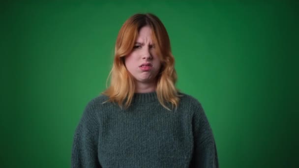Hoşnut olmayan kızıl saçlı kadın, gelişigüzel giyinmiş, yeşil zemine karşı kararlı bir ifadeyle hayır diyor. Tatminsizlik ifadesi reddedildiğini gösteriyor.. - Video, Çekim