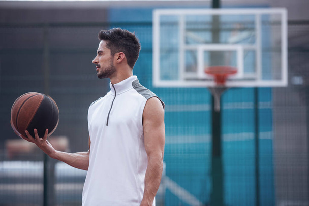 Guapo jugador de baloncesto está sosteniendo una pelota mientras está de pie en la cancha de baloncesto al aire libre
 - Foto, imagen