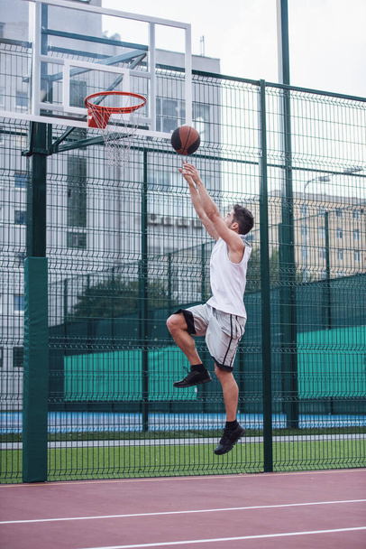 Bel giocatore di basket sta sparando una palla attraverso un cerchio mentre gioca sul campo da basket all'aperto
 - Foto, immagini