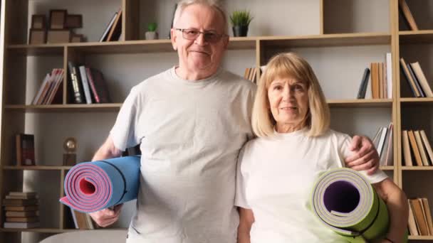 An elderly couple is preparing for a fitness workout, they are holding sports mats in their hands. - Footage, Video
