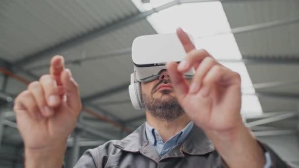 Kamera görüntüsü, kulaklıklı beyaz adam fabrikada imalat ürünleri görselleştiriyor. Üretken işler için VR gözlükleri kullanan bir mühendis. Üretim 3 boyutlu vizyon yardımıyla. Teknoloji yeniliği. - Video, Çekim
