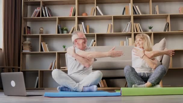 Активная пожилая пара делает упражнения и смотрит онлайн упражнения на ноутбуке в гостиной дома. Фитнес.  - Кадры, видео