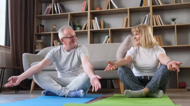 Happy healthy elderly 60s couple having fun, learning to meditate, at home, doing fitness training sports exercises. - Footage, Video