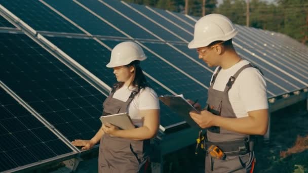 Central solar con dos ingenieros en ropa de trabajo protectora con herramientas que caminan y examinan paneles fotovoltaicos. Concepto de energía alternativa y su mantenimiento. Imágenes de alta calidad 4k - Metraje, vídeo