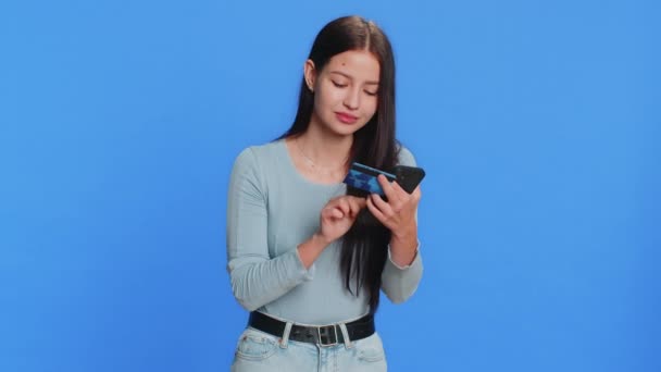 Happy Caucasian jonge vrouw met behulp van creditcard en smartphone tijdens het overmaken van geld uitgeven, online winkelen, het bestellen van voedsel levering. tiener mooi meisje geïsoleerd op blauwe achtergrond - Video