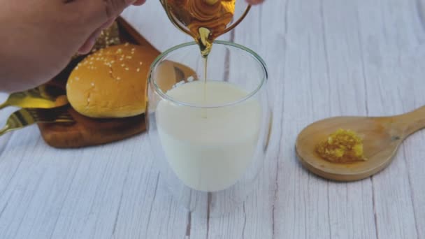 La mano di un uomo versa il miele in un bicchiere di latte. - Filmati, video