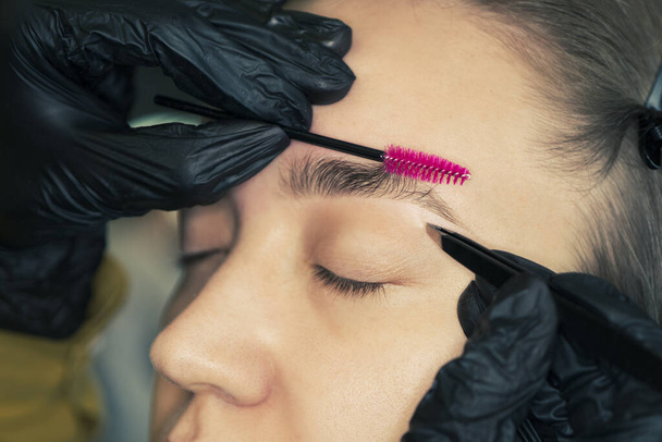Eyebrow correction. Perfect natural eyebrows and eyelashes. Lush eyebrow. Natural make up. Beauty. Eyebrow and eyelashes close up. Master cosmetologist removes excess eyebrows in the clinic - Photo, Image
