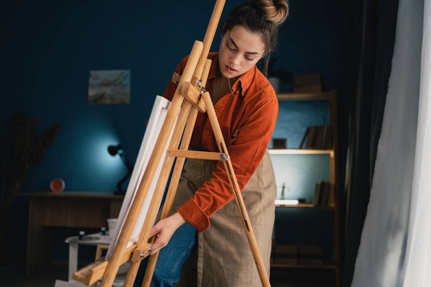 Luova latinonainen taiteilija seisoo uuden maalauksen kimpussa. Onnellinen nuori nainen maalaamassa kankaalle hänen taidestudiossaan. Taiteilija työskentelee kotona työpajassa. Kopioi tila - Valokuva, kuva